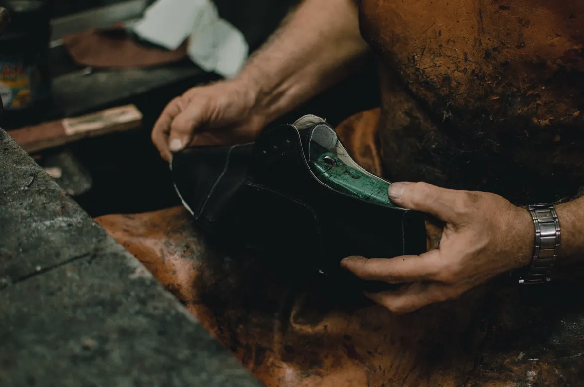Hands finishing a black leather shoe at a workbench